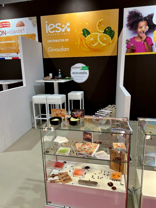 Stand IES Ingredients au salon professionnel avec vitrine d'échantillons d'ingrédients naturels et logo Givaudan