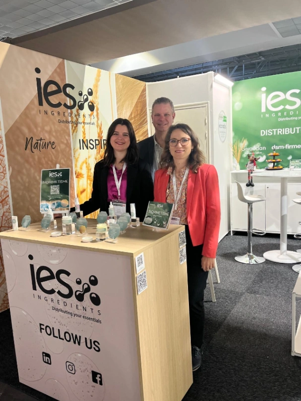 Équipe IES Ingredients au stand salon professionnel - 3 personnes souriantes devant présentoir produits naturels