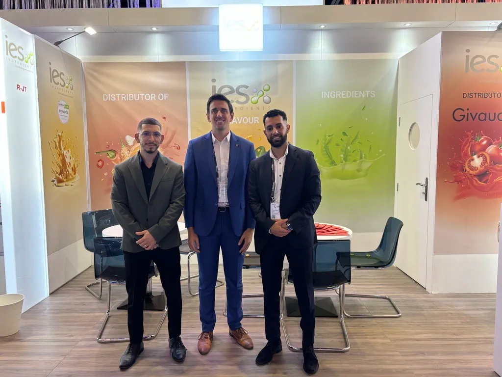 Équipe IES Ingredients sur stand salon professionnel - trois hommes en costume devant bannières colorées