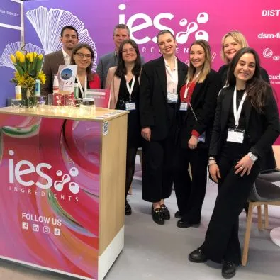 Équipe IES Ingredients au stand d'exposition avec logo entreprise et fleurs jaunes