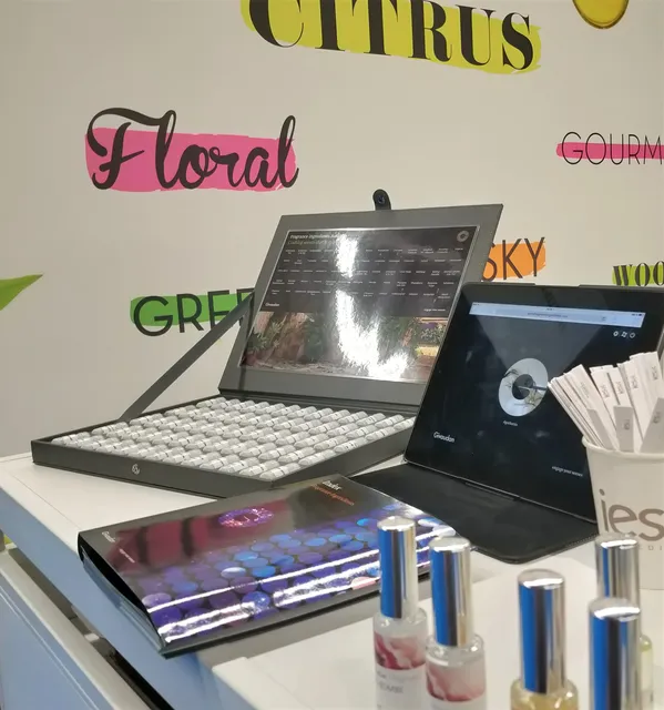 Laptops displaying fragrance analysis software with perfume bottles and scent classification wheel on laboratory desk