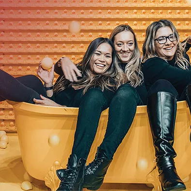 Trois femmes souriantes assises ensemble dans un environnement moderne avec mur en bois perforé