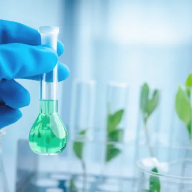 Main gantée tenant une fiole avec liquide vert en laboratoire, plantes en arrière-plan