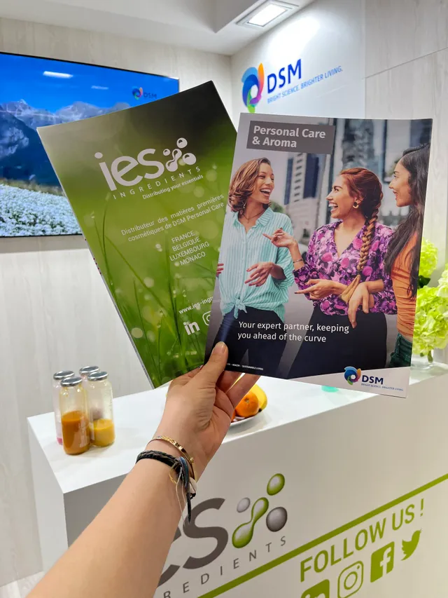 Hand holding IES Ingredients and DSM Personal Care brochures at a B2B professional trade show