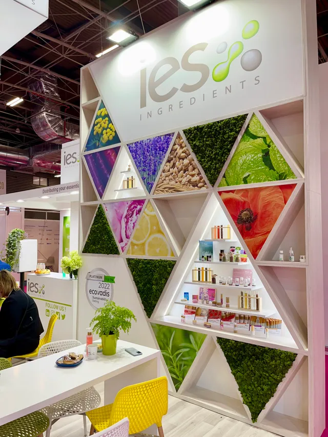 Stand IES Ingredients salon professionnel avec mur hexagonal coloré présentant ingrédients naturels cosmétiques