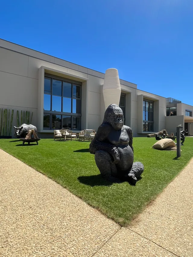 Sculpture moderne de gorille en bronze sur pelouse devant bâtiment contemporain avec grandes baies vitrées