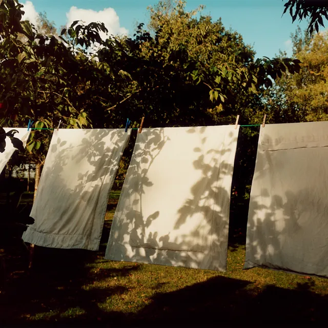 White laundry drying on a clothesline in a lush garden with tree shadows cast upon it